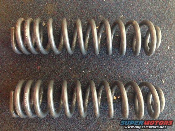 Two gray coil springs on a carpeted surface. Text is visible on the springs