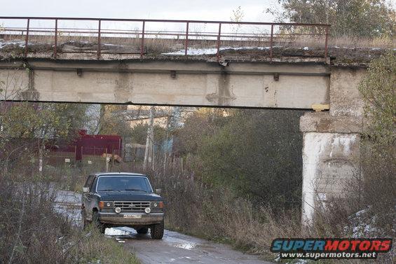 Black 1987 Ford Bronco parked on a dirt road under a concrete bridge, front-left view