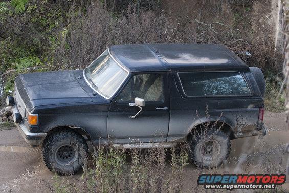 Black 1987 Ford Bronco driving through mud and brush