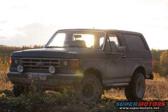 Dark 1987 Ford Bronco parked on a dirt road with a sunset in the background