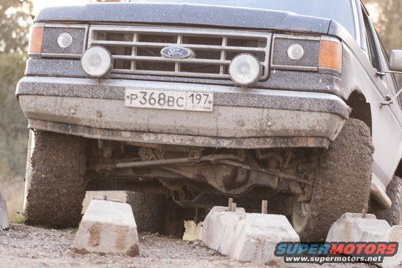 Front view of a muddy 1987 Ford Bronco with auxiliary lights mounted on the grille