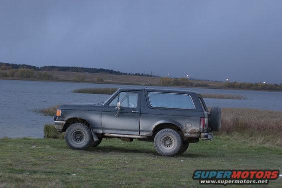 1987 Ford Bronco parked near water under a cloudy sky