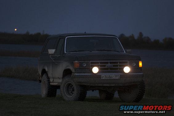 Dark SUV with headlights on, front view at dusk