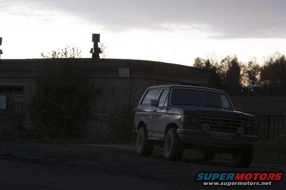 1987 Ford Bronco, dark color, front 3/4 view, slightly blurry, overcast sky