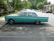 1964 Mercury Comet - A teal 1964 Mercury Comet sedan is parked in a lot with apartment buildings in the background.