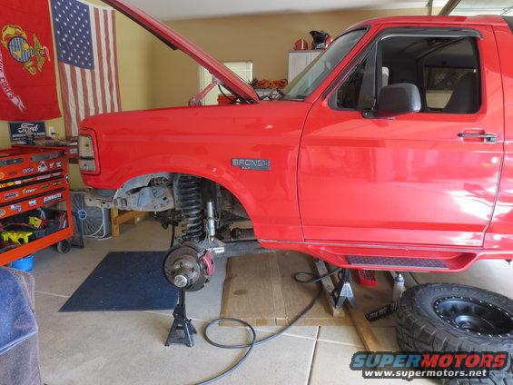 Red Ford Bronco on jack stands with hood open, front wheel removed