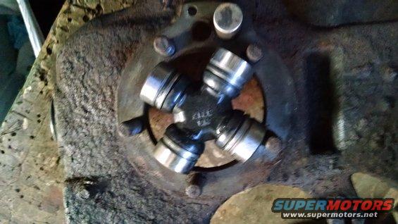 Close-up of a universal joint with four bearing caps, attached to a rusty flange