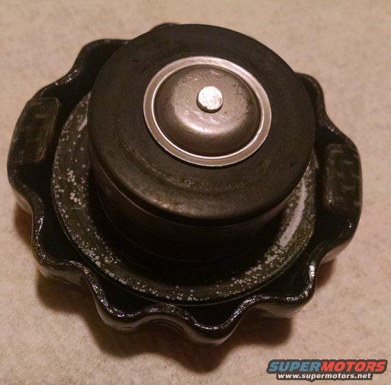 Radiator cap with a metal center and black rubber seal. Some white residue is visible on the black metal base