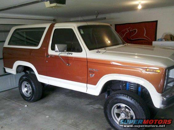 Two-tone brown and white Ford Bronco parked in a garage. It has aftermarket wheels and suspension