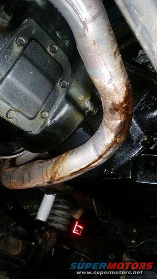 Underside view of vehicle exhaust pipe with rust and oil residue, near transmission housing