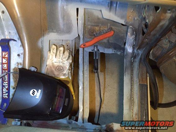 Miller welding helmet, work gloves, and wire brush on metal floor pans