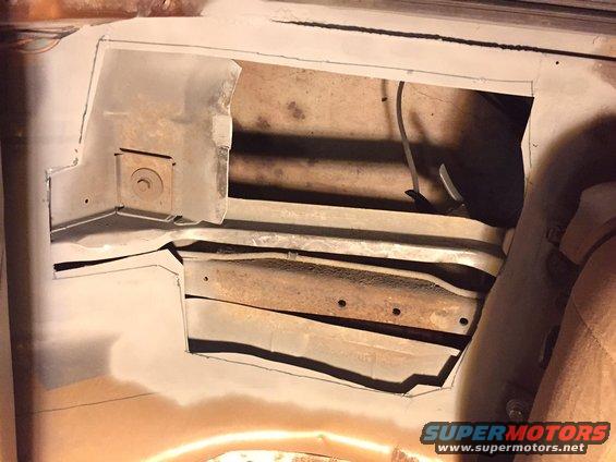 Cutout section of a rusted vehicle floor pan with exposed metal framing and wiring