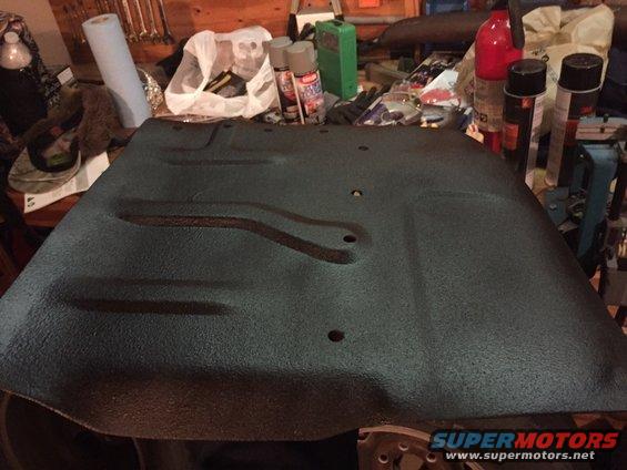 Black textured vehicle floor pan with stamped ribs and bolt holes