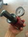 2014 Transnational Firestar 150CC - A hand holds a red gauge with a hex fitting and a pressure dial, likely a component for a tool or machine.