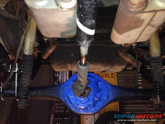 Underside view of a vehicle's rear axle and driveshaft, with dual exhaust pipes and mufflers visible