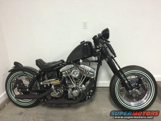 Black custom motorcycle with a V-twin engine, custom tank, and whitewall tires