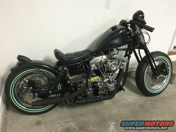 Black custom motorcycle with whitewall tires and exposed engine, viewed from the side