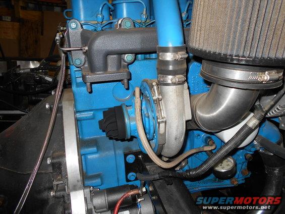 Close-up of a blue engine block with a silver turbocharger, black exhaust manifold, and air intake. A small gauge is visible