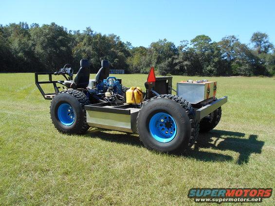 Custom off-road vehicle with two seats, large tires, and blue rims, parked on a grassy field
