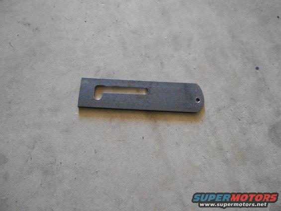 Metal bracket with a rectangular cutout and a rounded end with a hole, lying on a concrete surface