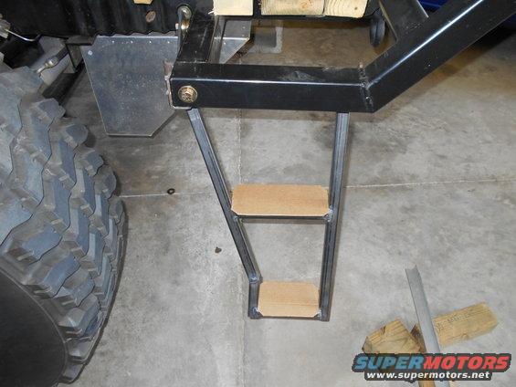 Close-up of custom metal steps with wooden treads attached to a vehicle's frame near a large tire