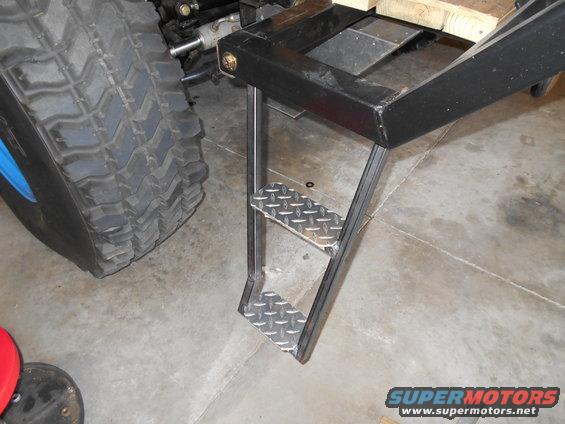 metal steps with diamond plate treads attached to a vehicle frame near a large tire