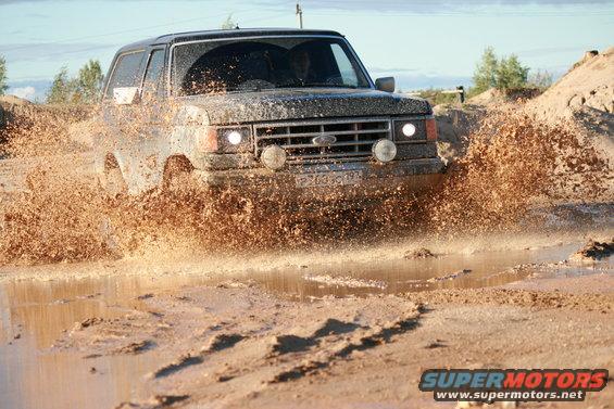 1987 Ford Bronco driving through mud, front view