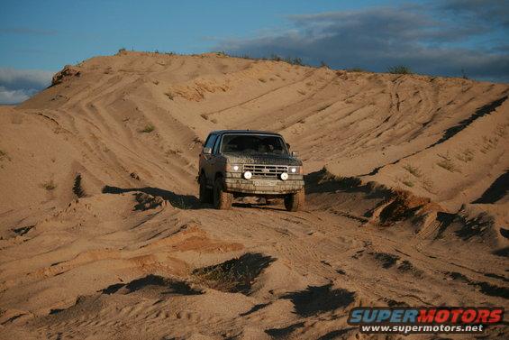 Ford Bronco driving up a sandy hill, covered in dust