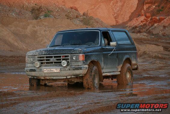 Dark blue 1987 Ford Bronco stuck in mud, front-left tire submerged