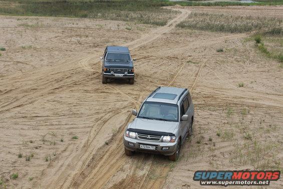 Two SUVs driving on sand dunes, one silver, one dark colored