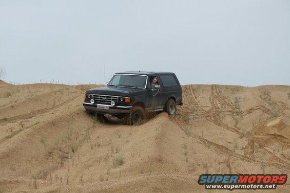 Black 1987 Ford Bronco driving on sand dunes, front-left view