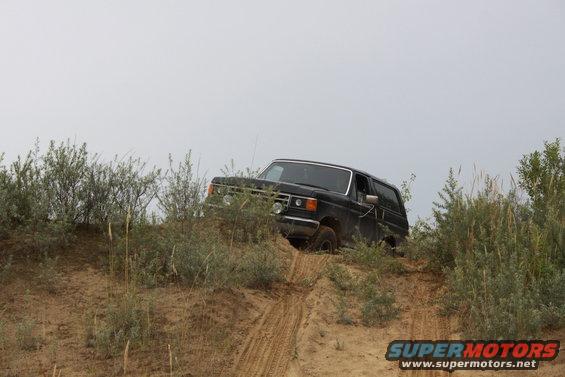 Black 1987 Ford Bronco driving up a sandy hill