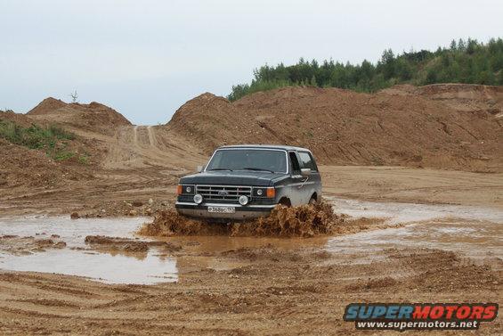 1987 Ford Bronco splashing through a muddy puddle in a dirt quarry
