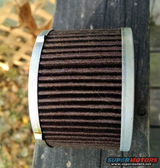 Oil filter with brown pleated media and metal end caps, resting on weathered wood