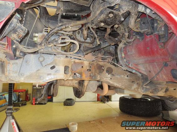 Red vehicle undercarriage with rusted frame, engine components, and exhaust system visible
