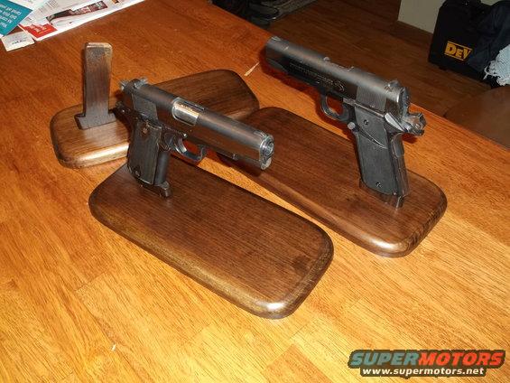 Two handguns on wooden display stands on a wooden table