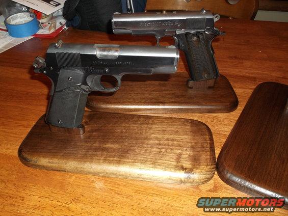 Two handguns displayed on wooden stands on a wooden table