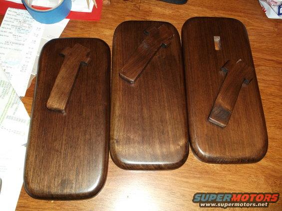 Three wooden blocks with T-shaped wooden pieces attached, on a wooden surface. Receipts and tape are visible in the background