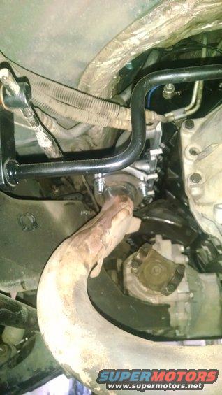 Underbody view of exhaust pipe and drivetrain components with Supermotors.net watermark