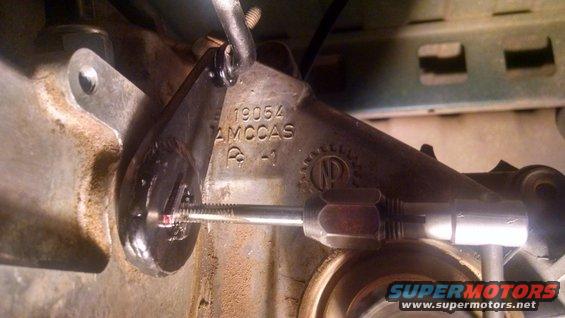 Close-up of metal linkage with stamped numbers 19054 AMCCAS and a gear-like symbol