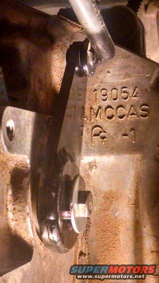 Close-up of a metal linkage with stamped numbers 19054 MCCAS and a symbol