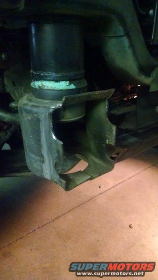 close-up of damaged metal bracket and black cylinder on vehicle underside