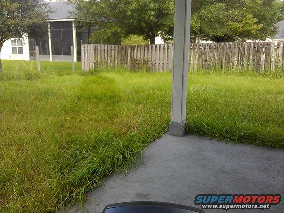 Backyard with overgrown grass, wooden fence, and a concrete patio with a support column