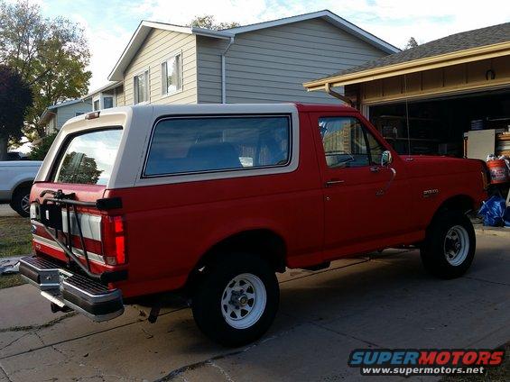 Red and white Ford Bronco parked in driveway, side view. White removable hardtop