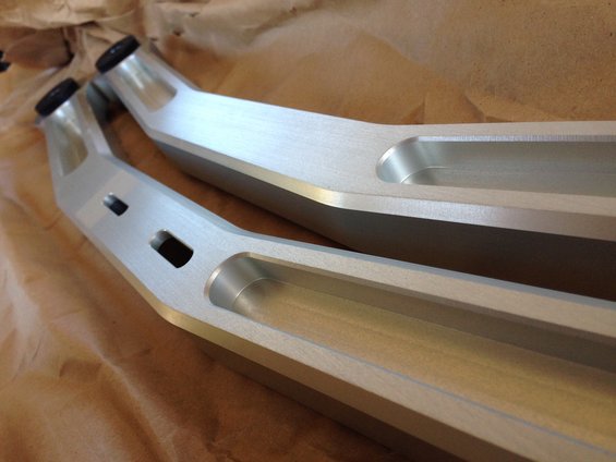 Two silver aluminum control arms with black end caps, resting on brown paper