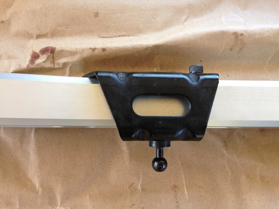 Close-up of a black metal bracket with an oval cutout attached to a silver bar, resting on brown paper