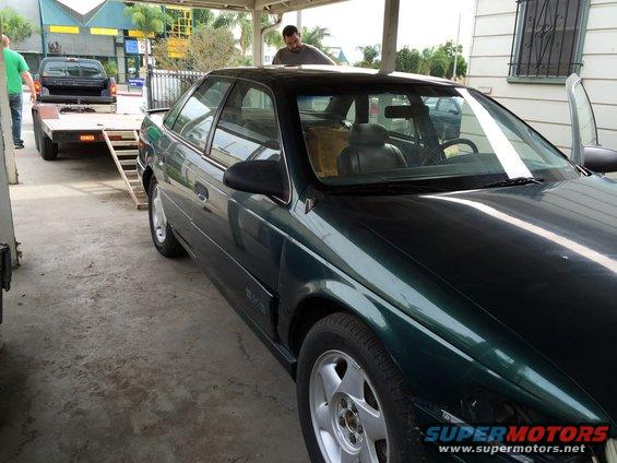 1993 Ford Taurus sedan parked under a carport, with a pickup truck and trailer visible behind it