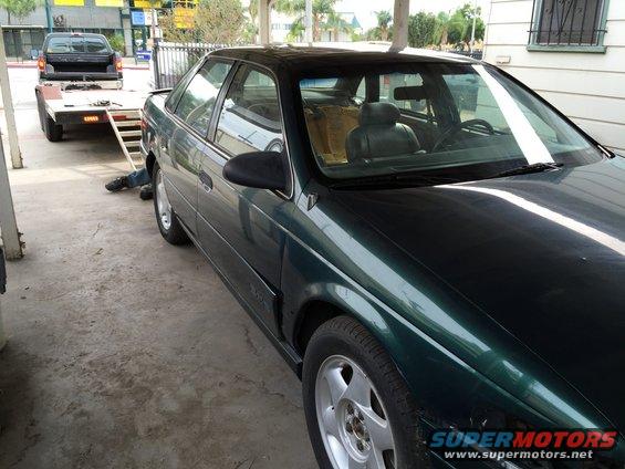 Dark green sedan, 1995 model year, parked next to a trailer with a pickup truck