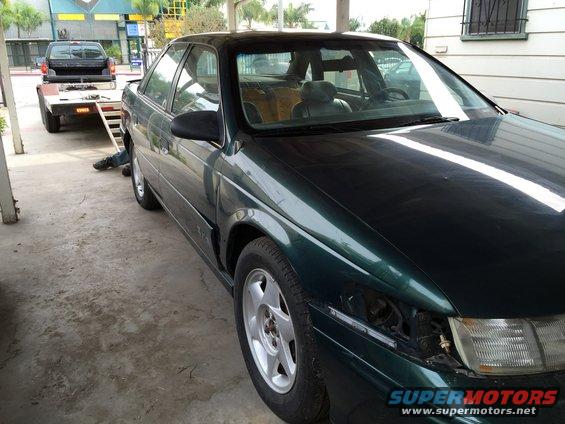Green 1993 Ford Taurus parked outside with a black pickup truck on a trailer in the background