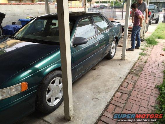 Green sedan parked under a carport. Two guys are standing nearby